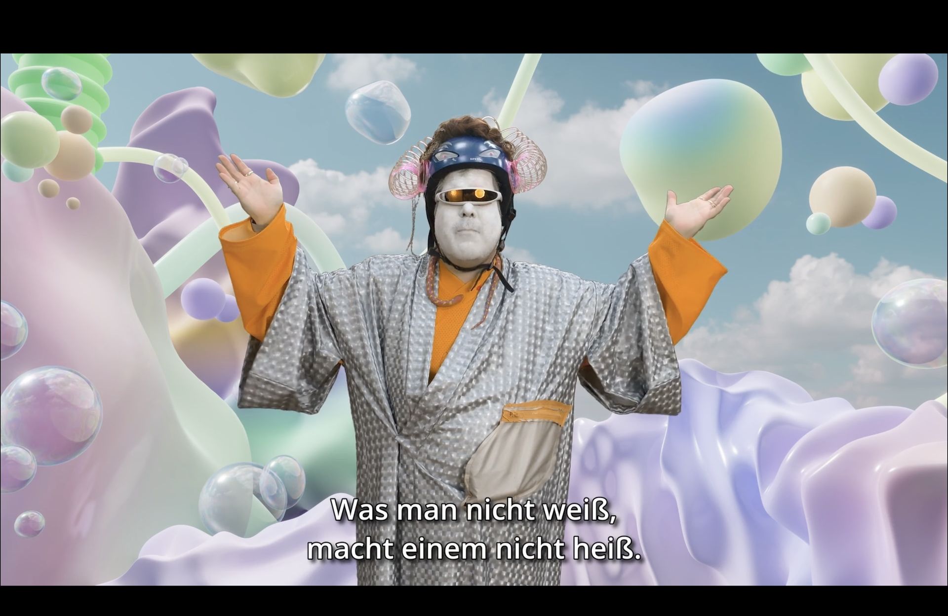 Das Foto zeigt einen Ausschnitt aus dem Film "Schule der Liebenden". Vor einem Hintergrund aus pastellfarbenen Formen steht ein Außerirdischer mit Laseraugen. Er sagt: "Was man nicht weiß, macht einem nicht heiß."